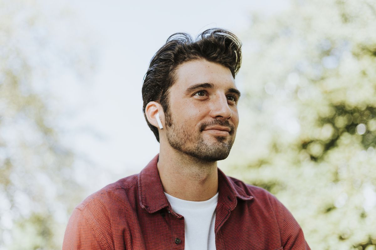 A man alone outdoors, looking away with earphones in